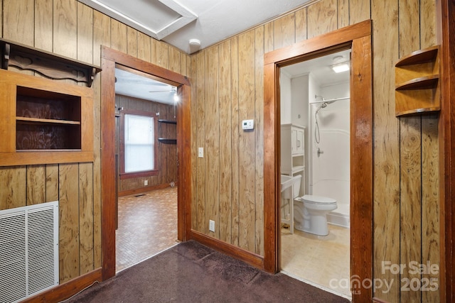 hallway featuring wood walls and dark carpet