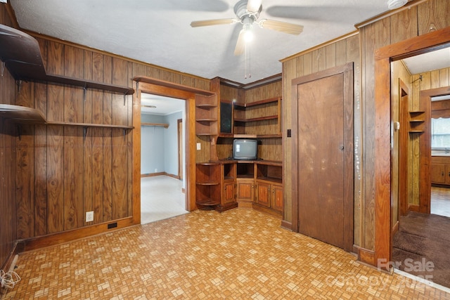 interior space featuring built in desk, wood walls, ornamental molding, and ceiling fan