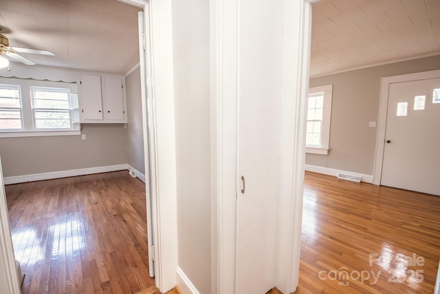 corridor with light wood-type flooring and crown molding