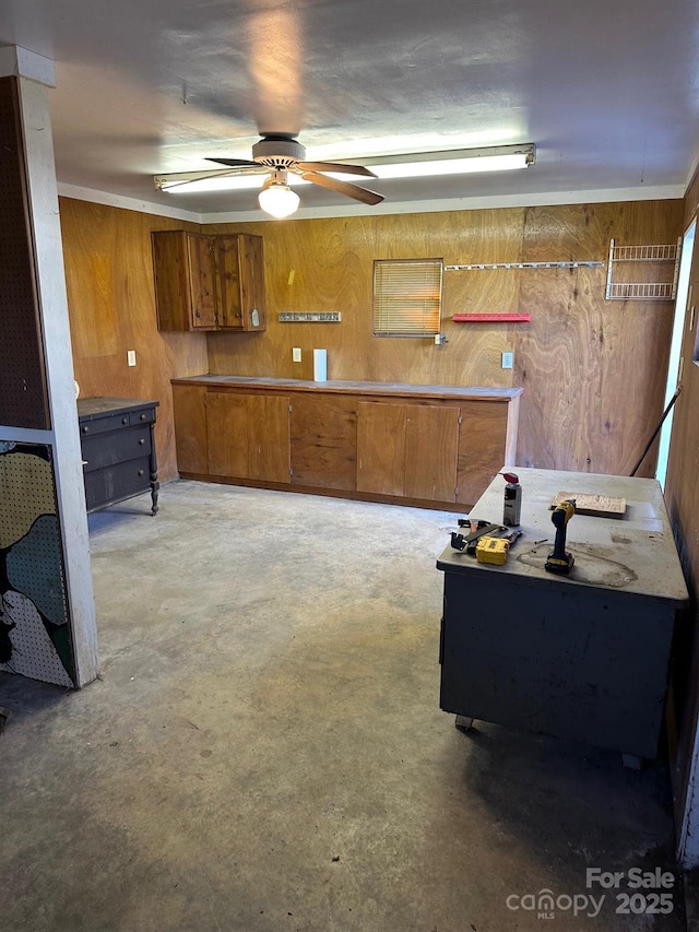 kitchen featuring wooden walls, ceiling fan, and concrete flooring