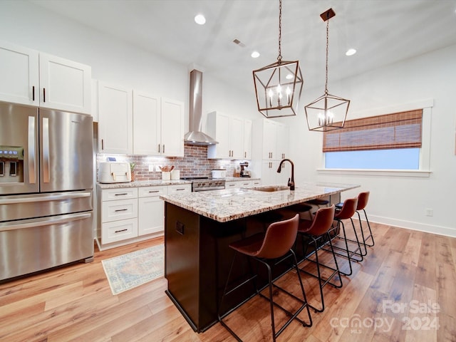 kitchen featuring a center island with sink, wall chimney range hood, sink, white cabinetry, and stainless steel appliances