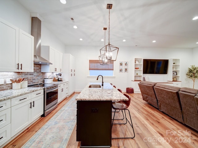 kitchen with wall chimney range hood, white cabinets, hanging light fixtures, and stainless steel range oven