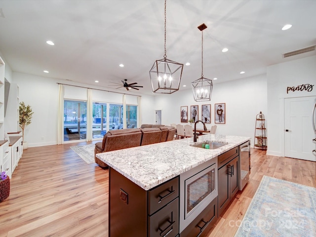 kitchen featuring light wood-type flooring, dark brown cabinets, ceiling fan, sink, and pendant lighting