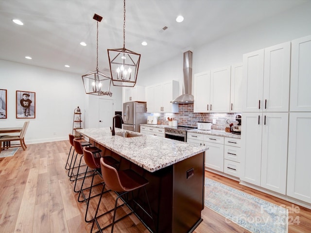 kitchen featuring a center island with sink, white cabinets, and wall chimney range hood