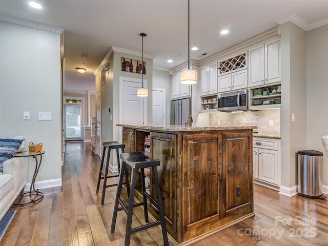 kitchen with pendant lighting, light stone counters, appliances with stainless steel finishes, and a center island with sink