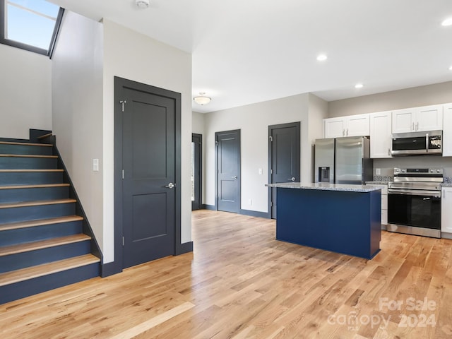 kitchen with light stone countertops, a kitchen island, light hardwood / wood-style flooring, white cabinets, and appliances with stainless steel finishes