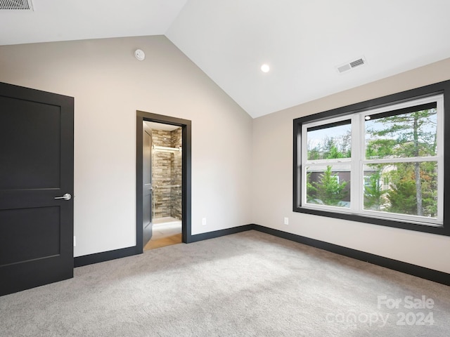 unfurnished bedroom featuring ensuite bath, light colored carpet, and lofted ceiling