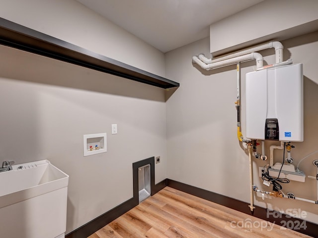 laundry area with sink, tankless water heater, hookup for an electric dryer, hookup for a washing machine, and hardwood / wood-style flooring