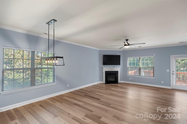 unfurnished living room with ceiling fan with notable chandelier, light wood-type flooring, and ornamental molding