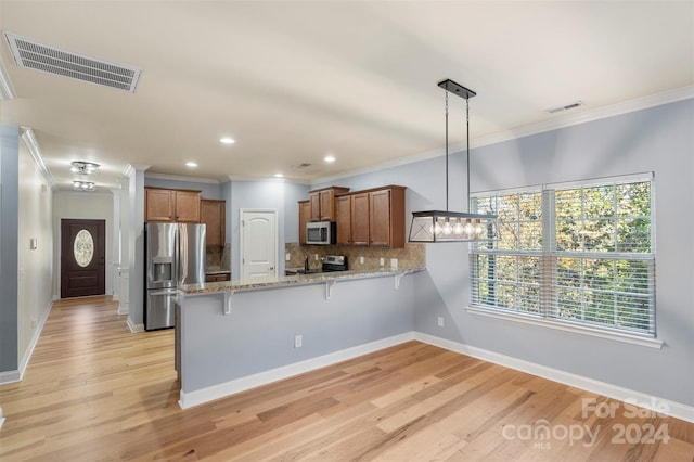 kitchen with kitchen peninsula, light stone counters, stainless steel appliances, light hardwood / wood-style floors, and hanging light fixtures