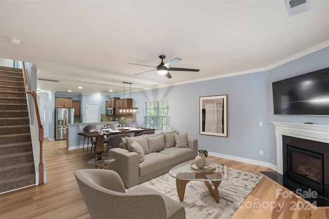 living room with ceiling fan, crown molding, and light hardwood / wood-style flooring