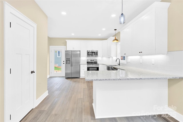 kitchen featuring light stone counters, kitchen peninsula, pendant lighting, white cabinets, and appliances with stainless steel finishes