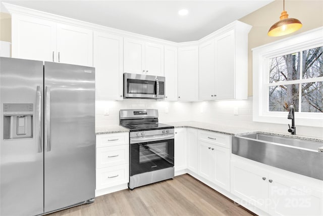 kitchen with stainless steel appliances, tasteful backsplash, a sink, and light wood-style floors