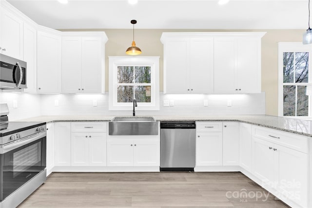 kitchen with appliances with stainless steel finishes, hanging light fixtures, white cabinetry, and sink