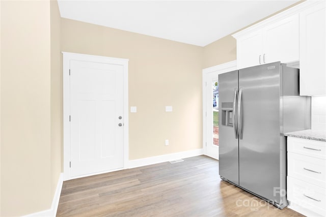 kitchen with light hardwood / wood-style floors, white cabinetry, light stone counters, and stainless steel refrigerator with ice dispenser