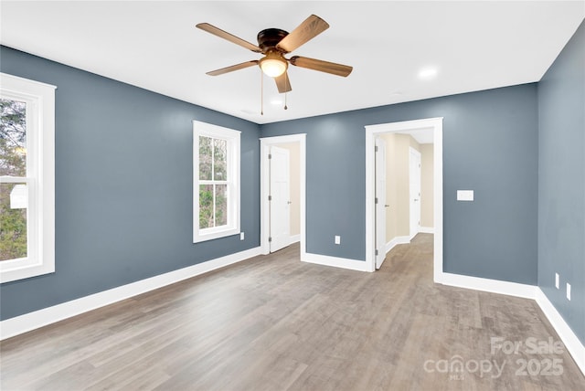 empty room with baseboards, ceiling fan, wood finished floors, and a healthy amount of sunlight