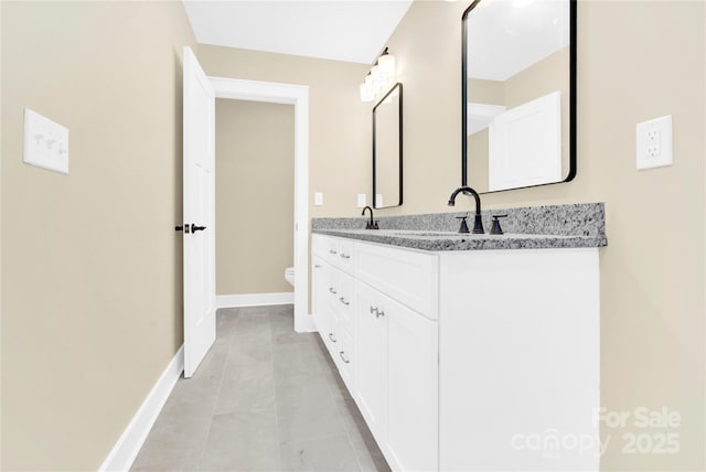 bathroom featuring baseboards, a sink, toilet, and double vanity