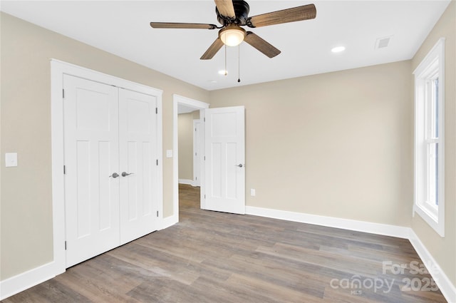 unfurnished bedroom featuring ceiling fan, wood finished floors, visible vents, baseboards, and a closet