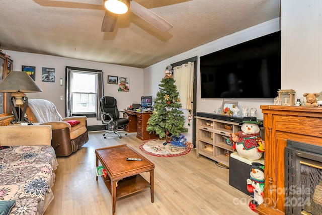 living room featuring ceiling fan, ornamental molding, a textured ceiling, and light hardwood / wood-style flooring