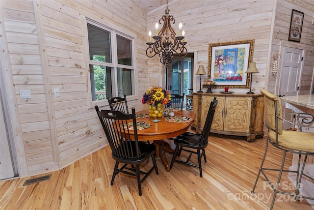 dining room with wood walls, an inviting chandelier, and light wood-type flooring