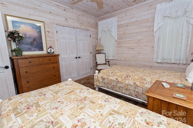 bedroom with ceiling fan, wood walls, wooden ceiling, and a closet