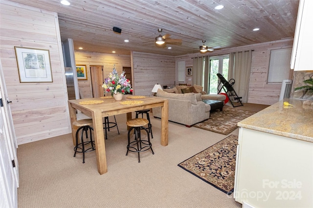 dining space with wooden walls, ceiling fan, wood ceiling, and light carpet