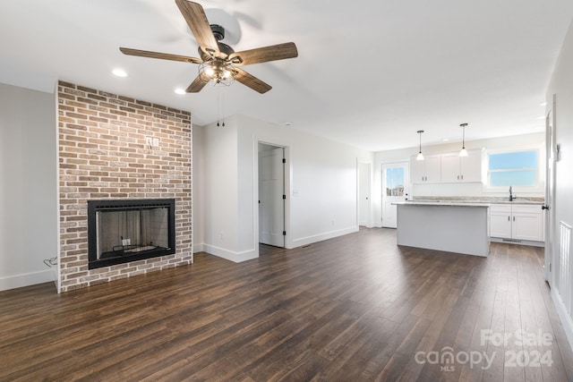 unfurnished living room featuring ceiling fan, dark hardwood / wood-style flooring, sink, and a brick fireplace