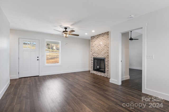 unfurnished living room featuring ceiling fan, dark wood-type flooring, and a brick fireplace