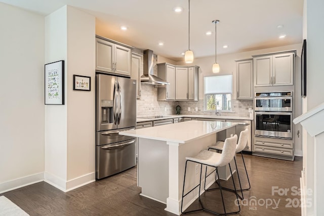 kitchen featuring gray cabinetry, a center island, wall chimney range hood, appliances with stainless steel finishes, and a breakfast bar area