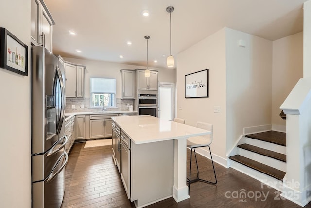 kitchen with gray cabinetry, decorative backsplash, a kitchen island, and appliances with stainless steel finishes