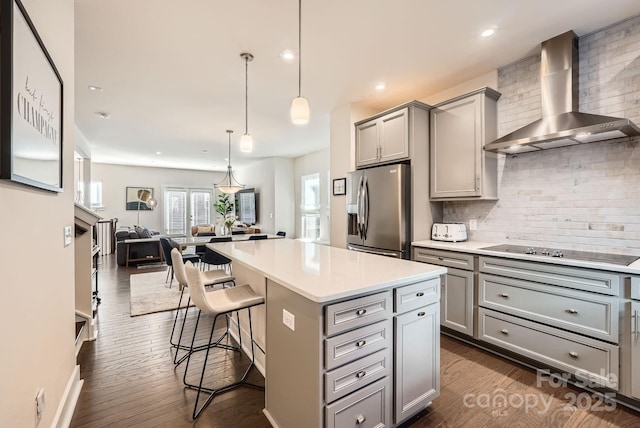 kitchen with gray cabinetry, a center island, wall chimney range hood, stainless steel fridge, and decorative light fixtures