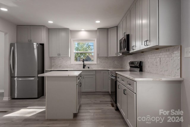 kitchen with sink, light hardwood / wood-style flooring, decorative backsplash, a kitchen island, and appliances with stainless steel finishes