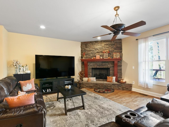 living room with hardwood / wood-style flooring, a stone fireplace, and ceiling fan