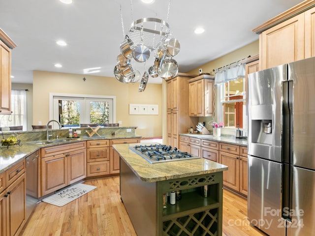 kitchen with light stone counters, stainless steel appliances, sink, a center island, and light hardwood / wood-style floors