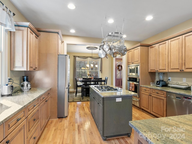 kitchen with appliances with stainless steel finishes, light stone counters, light hardwood / wood-style flooring, a kitchen island, and hanging light fixtures