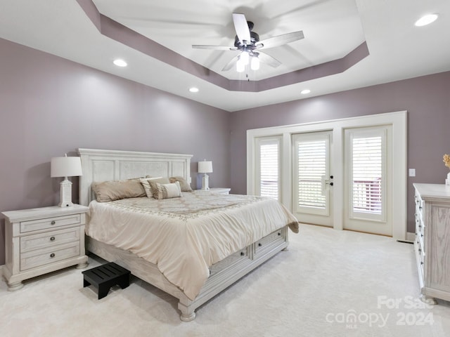 bedroom with a raised ceiling, ceiling fan, light carpet, and access to outside