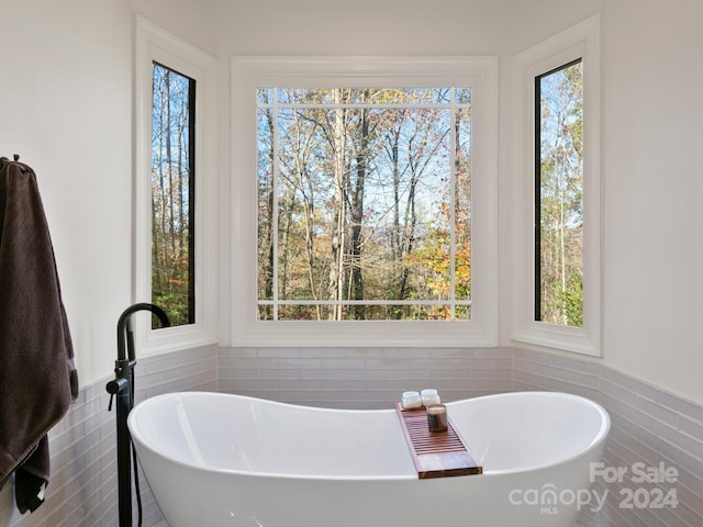 bathroom featuring a bathtub, a healthy amount of sunlight, and tile walls