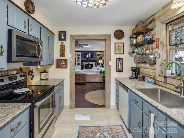 kitchen featuring stainless steel appliances, light wood-style flooring, a sink, blue cabinetry, and ceiling fan