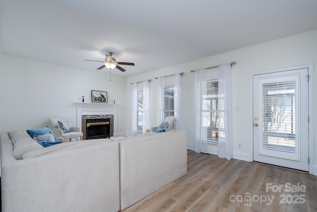 living room with wood-type flooring, ceiling fan, and a stone fireplace