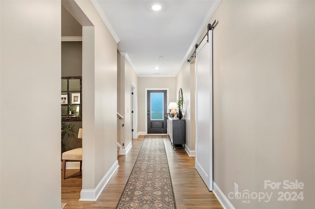 hallway featuring a barn door, wood-type flooring, and ornamental molding