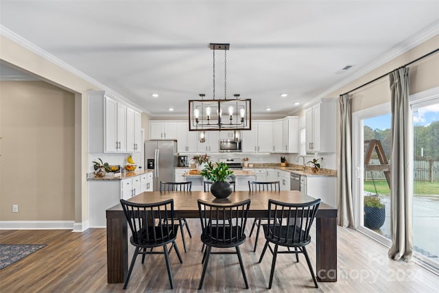 dining space with light wood-type flooring, an inviting chandelier, crown molding, and sink