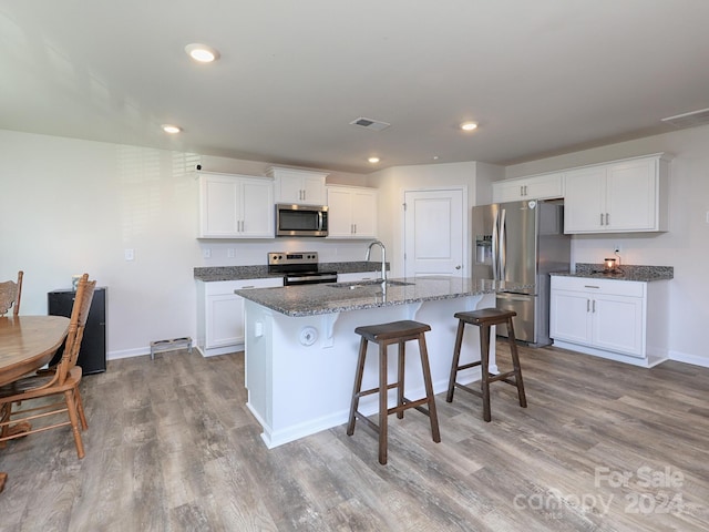 kitchen with white cabinetry, sink, stainless steel appliances, an island with sink, and light wood-type flooring