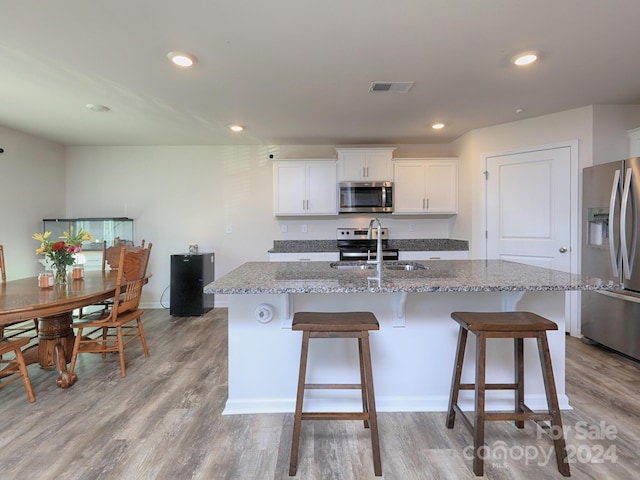 kitchen with white cabinets, sink, an island with sink, light hardwood / wood-style floors, and stainless steel appliances