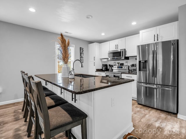 kitchen with a breakfast bar, sink, an island with sink, white cabinetry, and stainless steel appliances