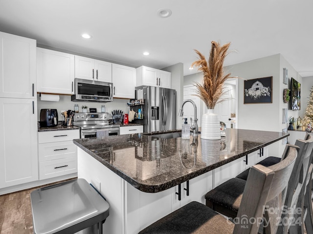 kitchen with appliances with stainless steel finishes, a center island with sink, and white cabinetry