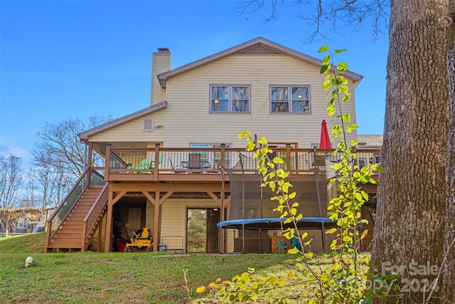 back of house with a trampoline, a lawn, and a wooden deck