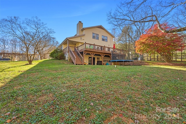 rear view of property with a trampoline, a deck, and a lawn