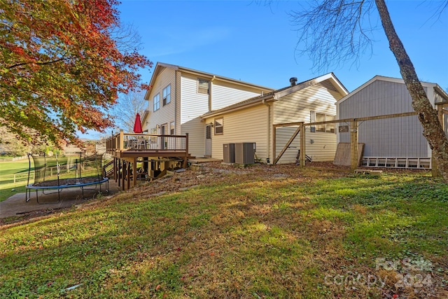 rear view of house featuring a deck, a trampoline, a yard, and central air condition unit