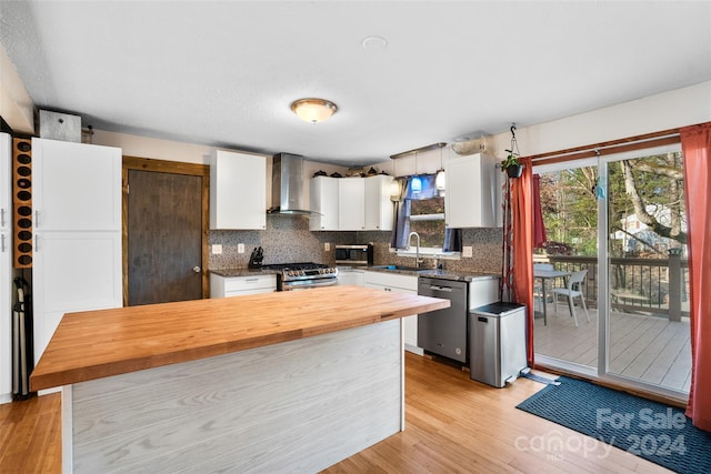 kitchen with wood counters, wall chimney exhaust hood, appliances with stainless steel finishes, light hardwood / wood-style floors, and white cabinetry