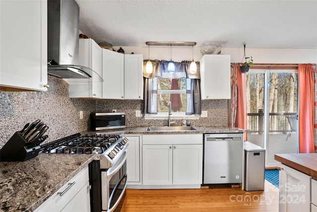 kitchen with sink, wall chimney range hood, decorative light fixtures, white cabinets, and appliances with stainless steel finishes